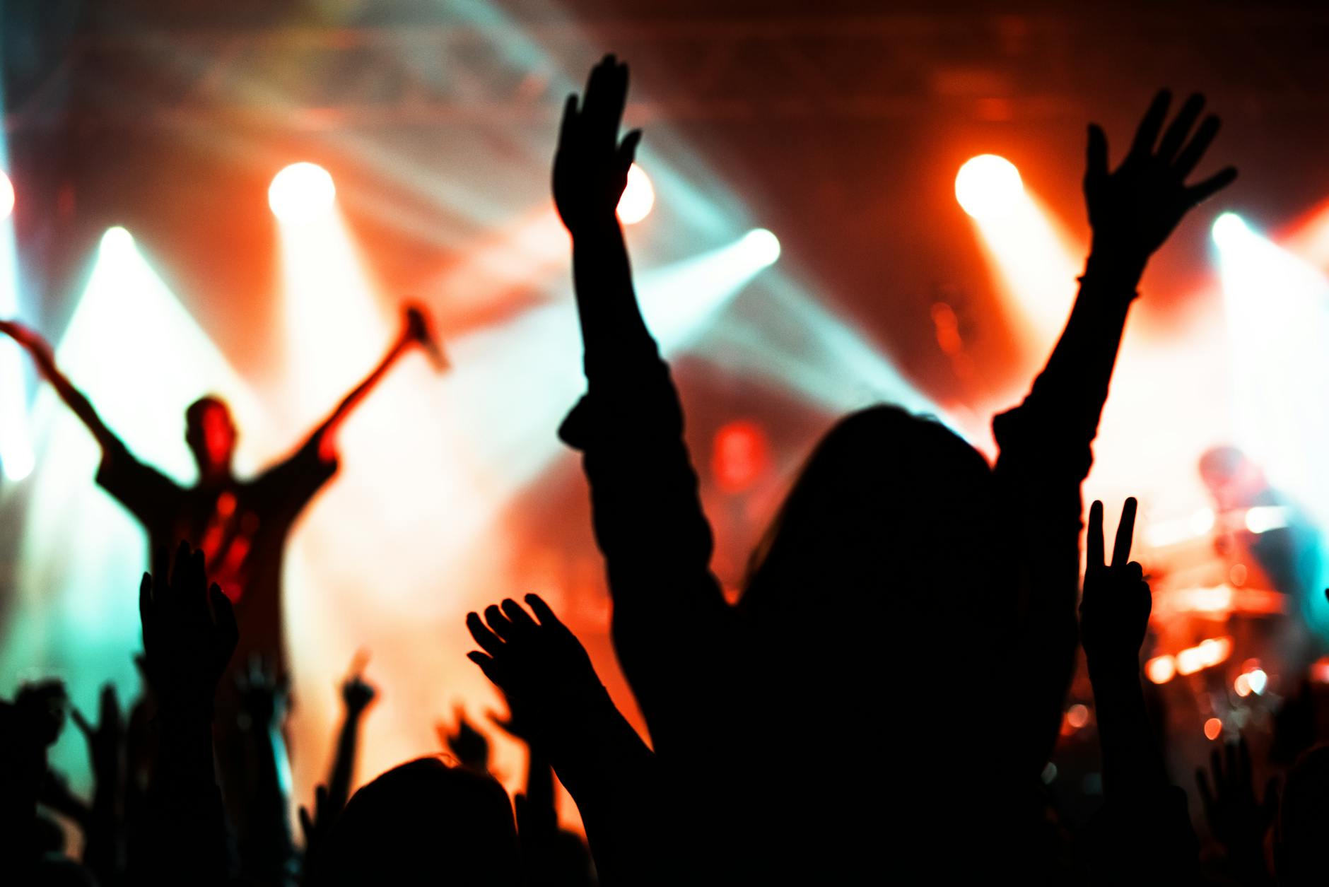 Silhouetted crowd at concert venue with raised hands against stage lighting